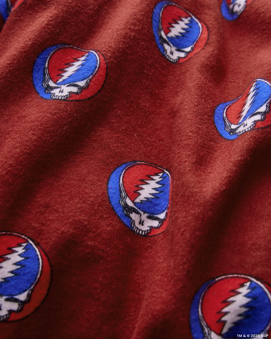 Close-up of red flannel pajama fabric with repeated skull-and-lightning-bolt emblems.