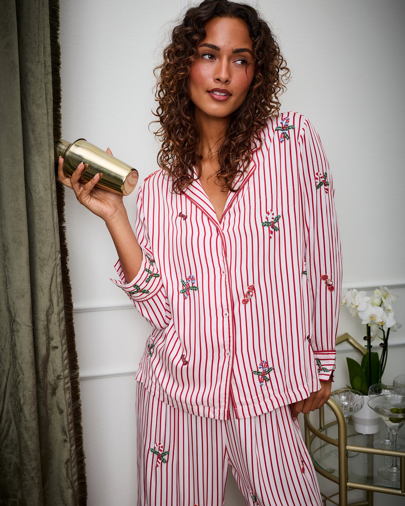 Close lifestyle view of the Sugar Stripe Ellie pajama set with red vertical stripes and decorative motifs, while the wearer holds a gold tumbler.