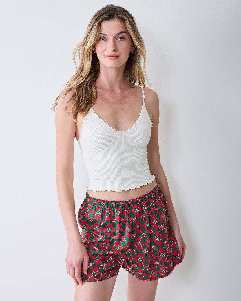 Three-quarter front view of red boxer shorts with a green argyle and bow print on a model.