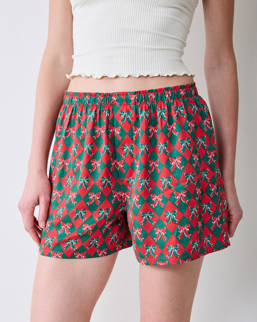 Back view of red boxer shorts with a green argyle pattern and bow motifs, shown on a model.