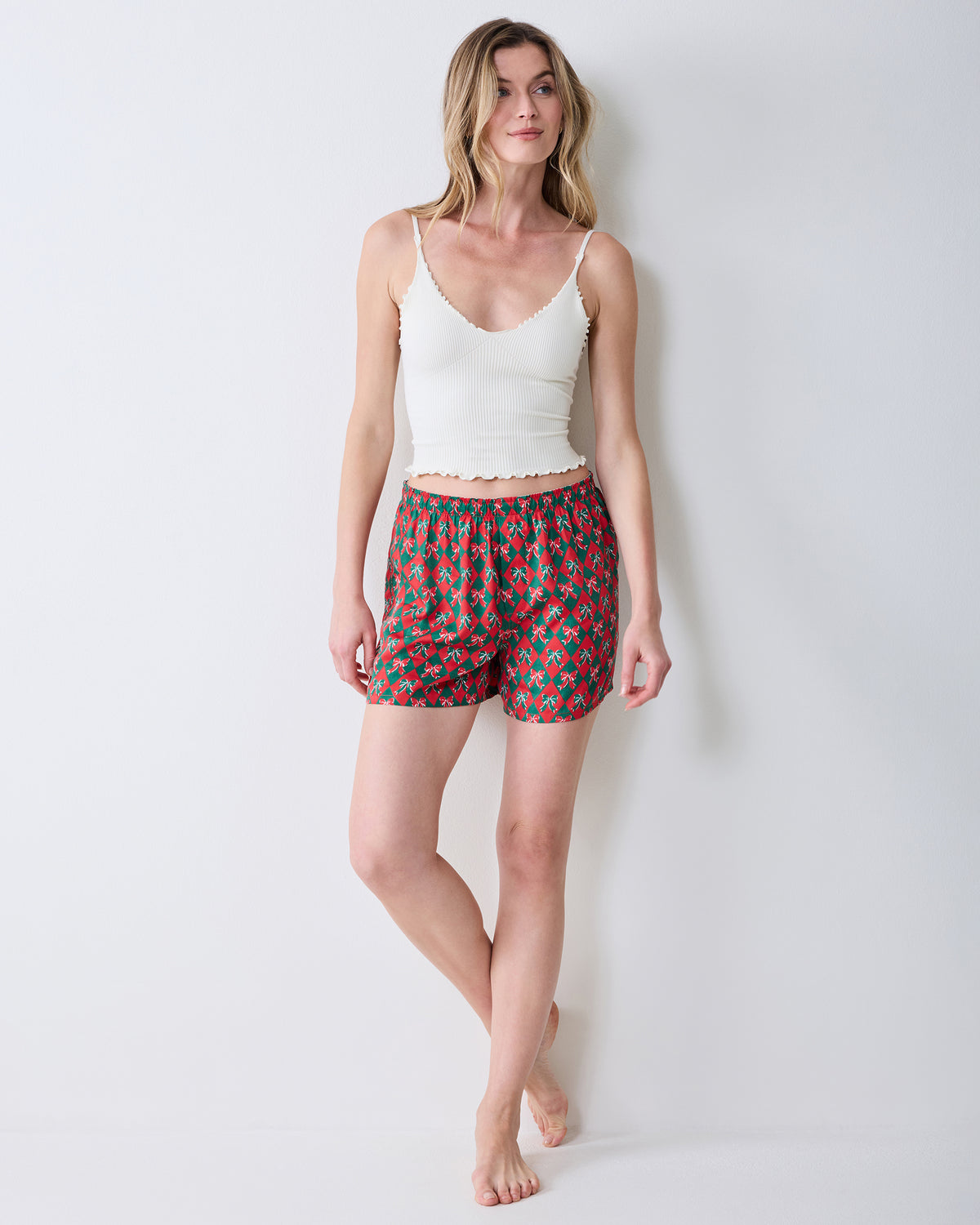 Angled front view of red boxer shorts with a green argyle and bow print on a model.