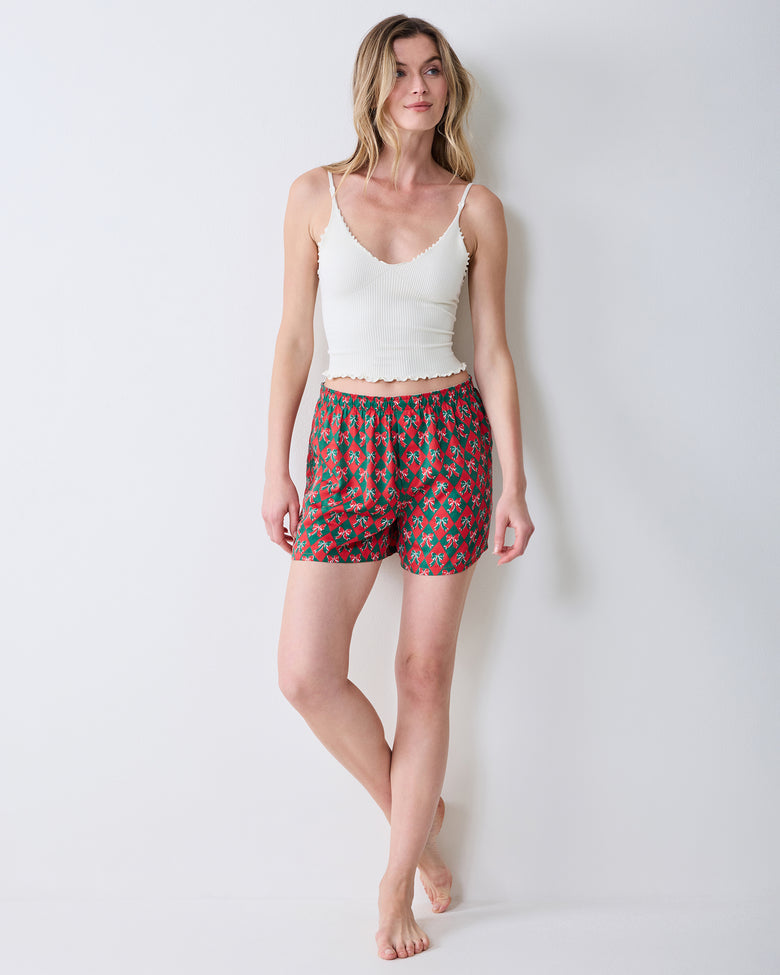 Angled front view of red boxer shorts with a green argyle and bow print on a model.