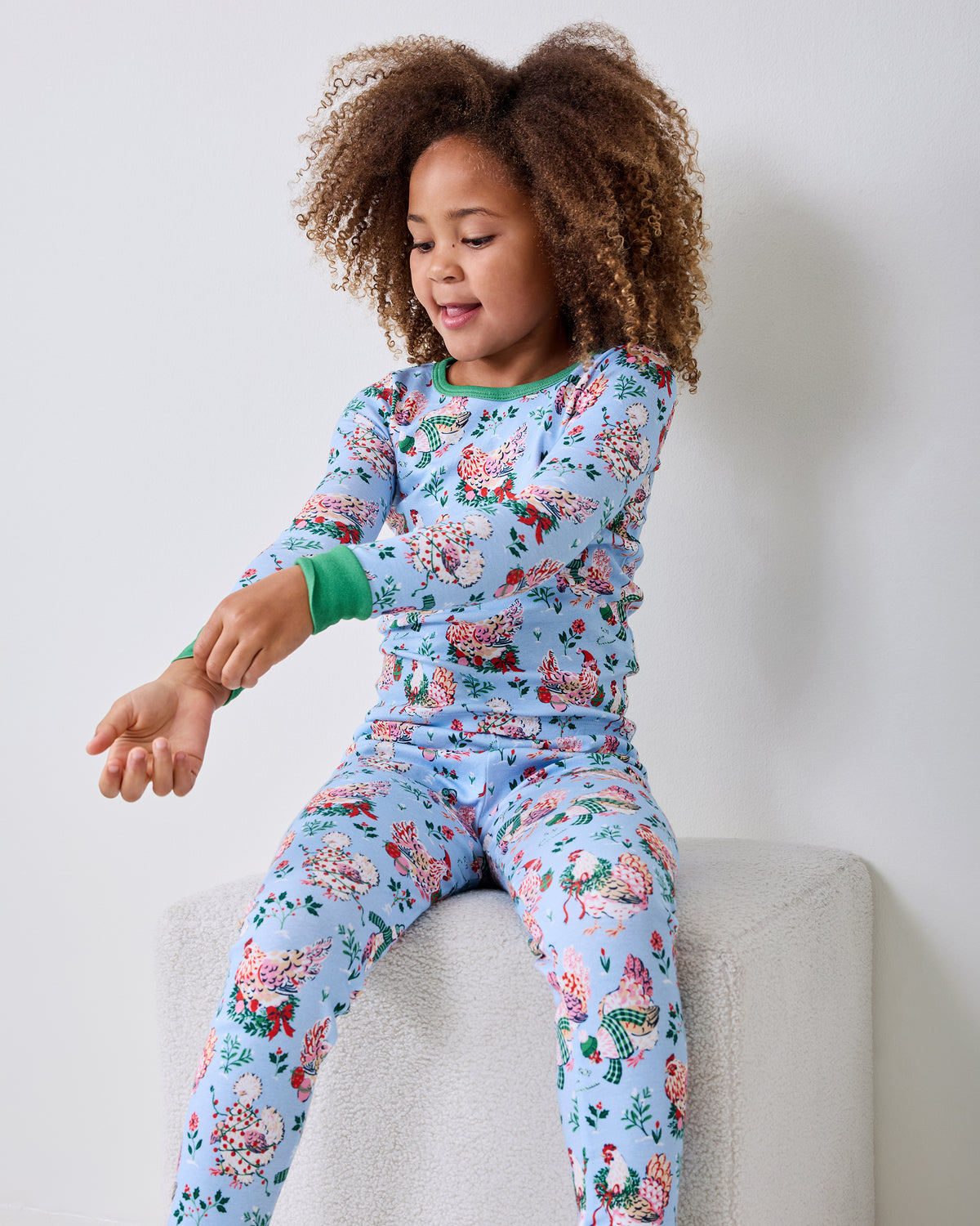 Child seated on a bench wearing a light blue long-sleeved pajama set with a floral and bird pattern.