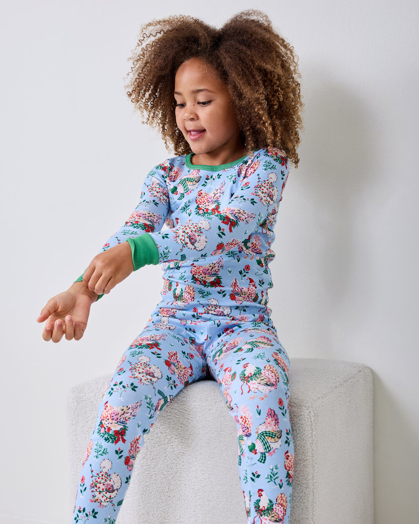 Child seated on a bench wearing a light blue long-sleeved pajama set with a floral and bird pattern.