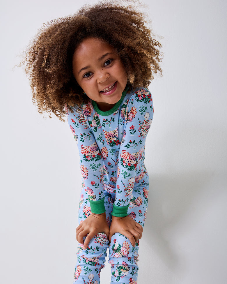 Child wearing a pale blue Holiday Hens long pajama set stands against a light wall with hands on their knees.