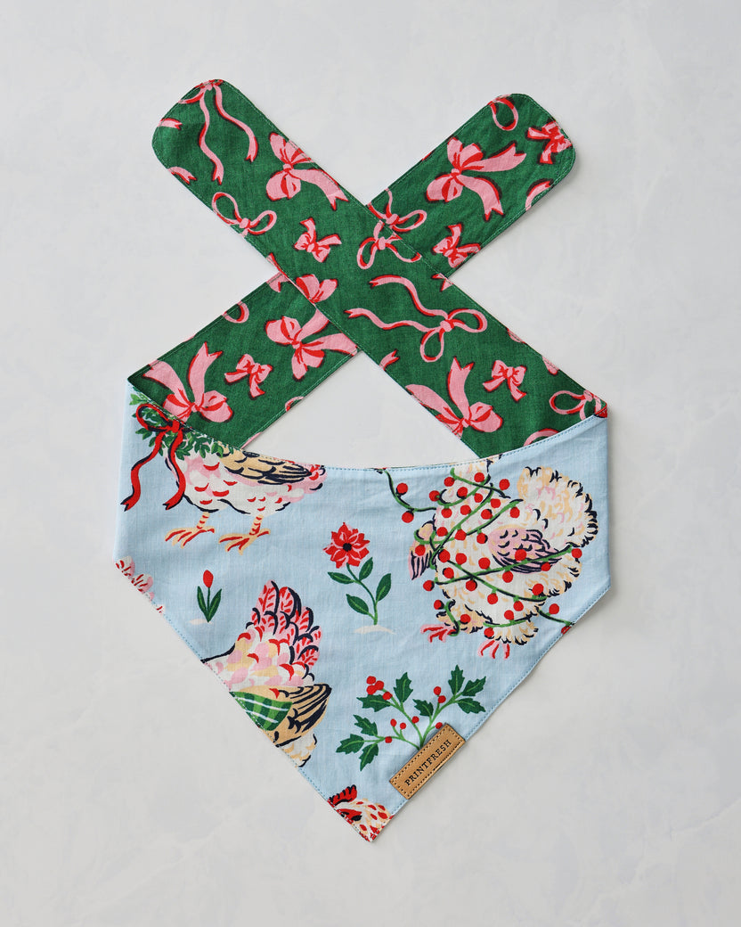 Pale blue pet bandana with floral and hen print, shown close up with a brand tag.