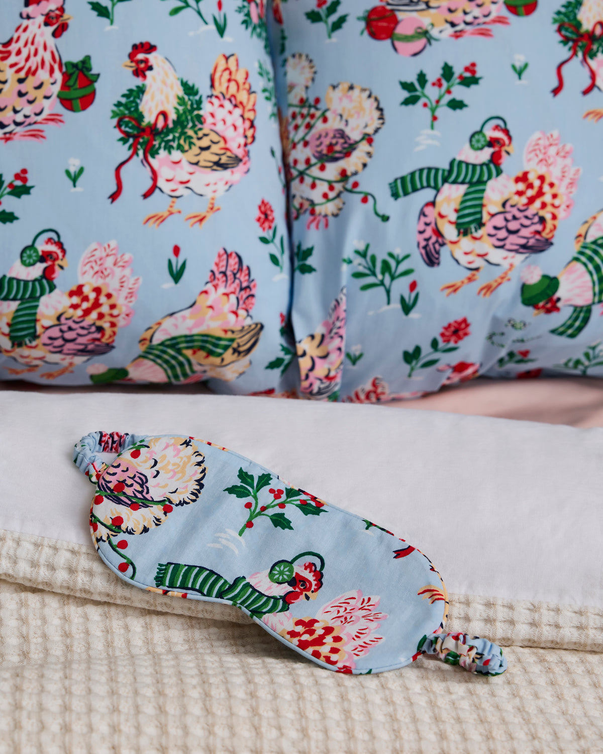 Close-up of the pale blue Holiday Hens pillowcase print with a matching sleep mask in the foreground.