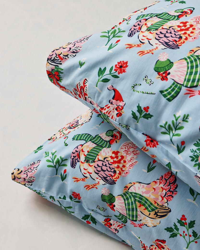Close-up of two pale blue Holiday Hens pillowcases showing the printed hen design and finished edges.