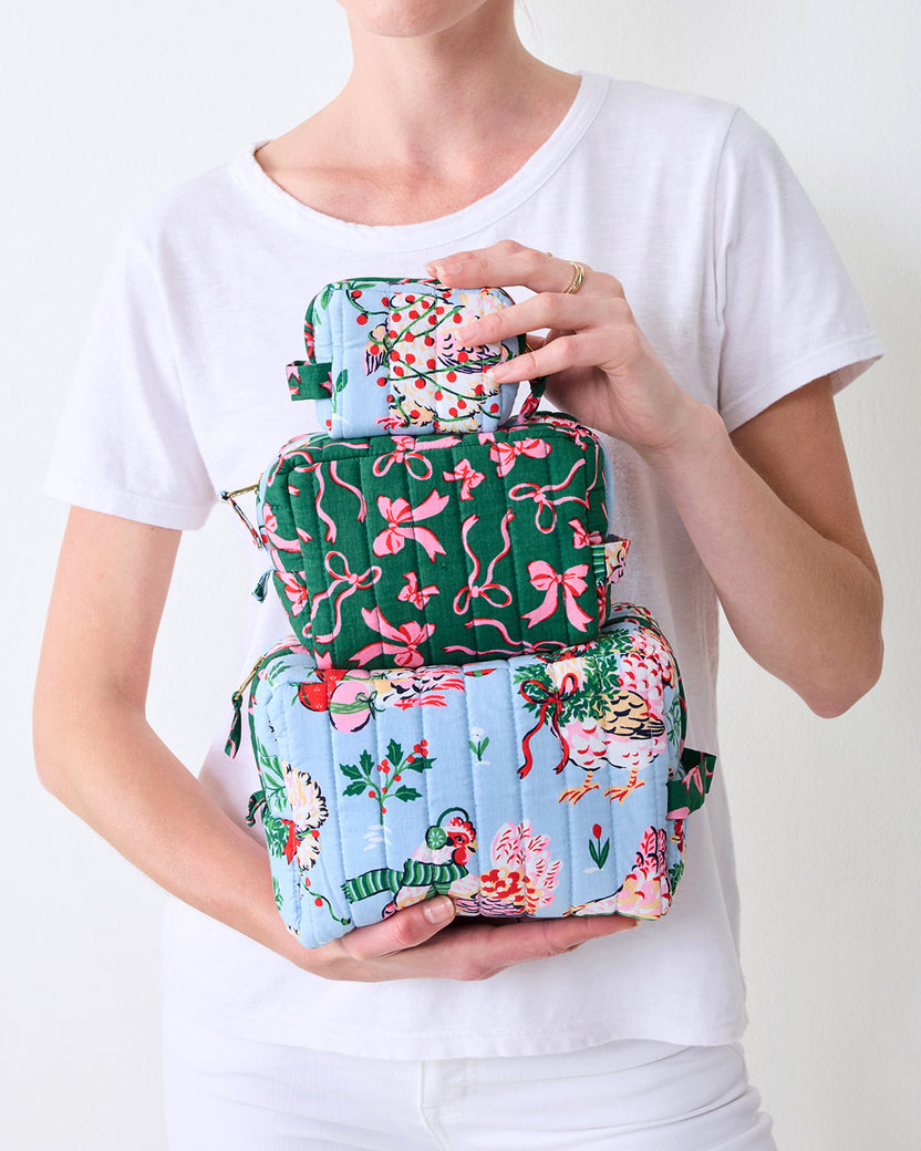 Person holding all three quilted pouches in the pale blue Holiday Hens set, stacked by size and showing the contrasting hen and pink bow prints.