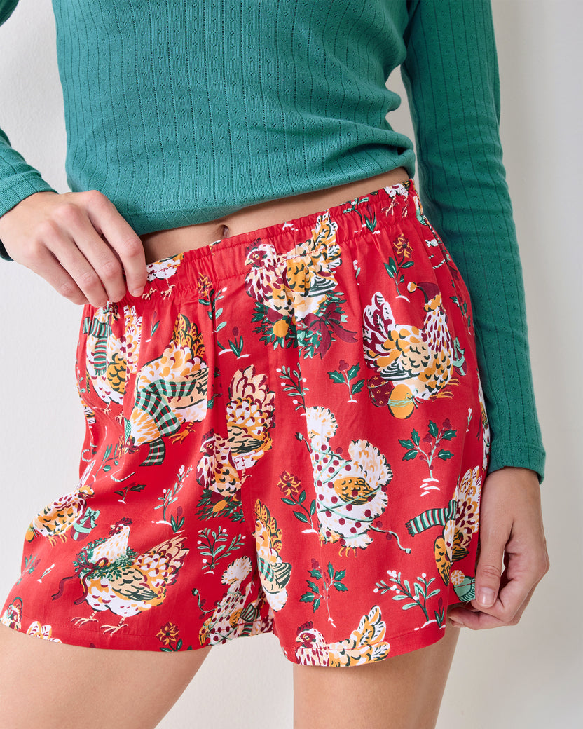 Red boxer shorts with a repeating holiday chicken print, shown worn with a teal ribbed top.