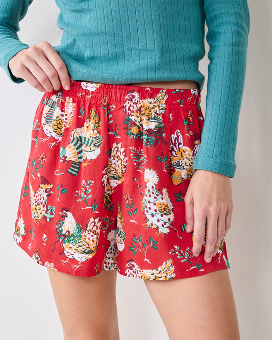 Close-up front view of red Holiday Hens boxer shorts with an elastic waistband and chicken print, worn with a teal long-sleeve top.