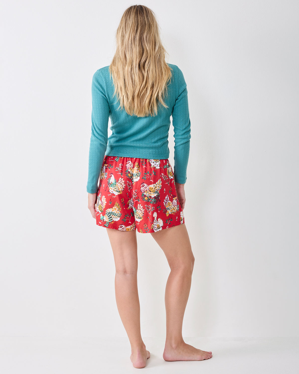 Back view of a person wearing red Holiday Hens printed boxer shorts with a teal long-sleeve top.