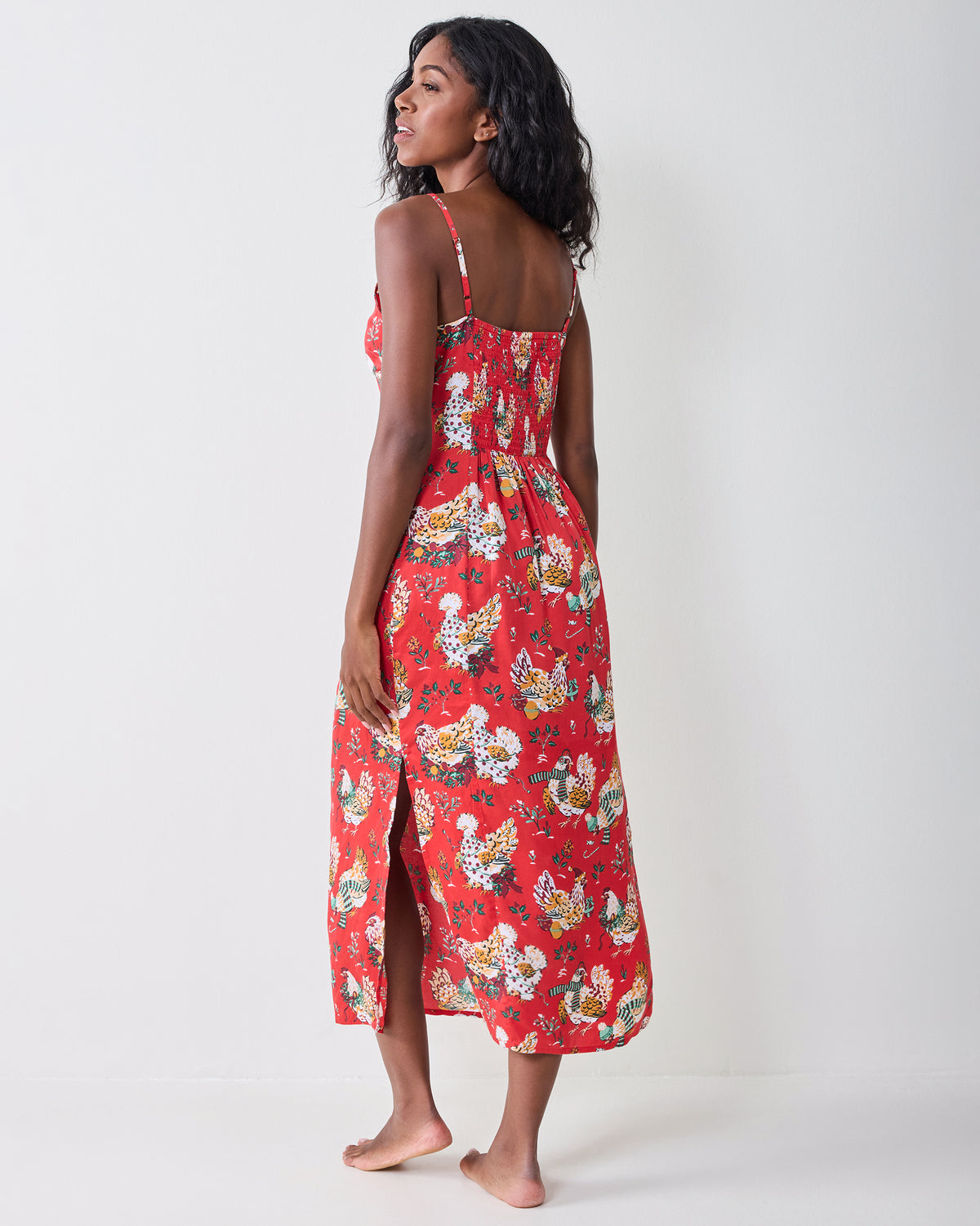 Back view of a model wearing the red Holiday Hens nightie, showing thin adjustable straps, a smocked back, and a side slit.