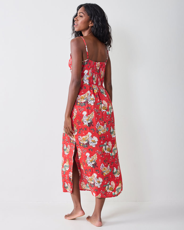 Back view of a model wearing the red Holiday Hens nightie, showing thin adjustable straps, a smocked back, and a side slit.