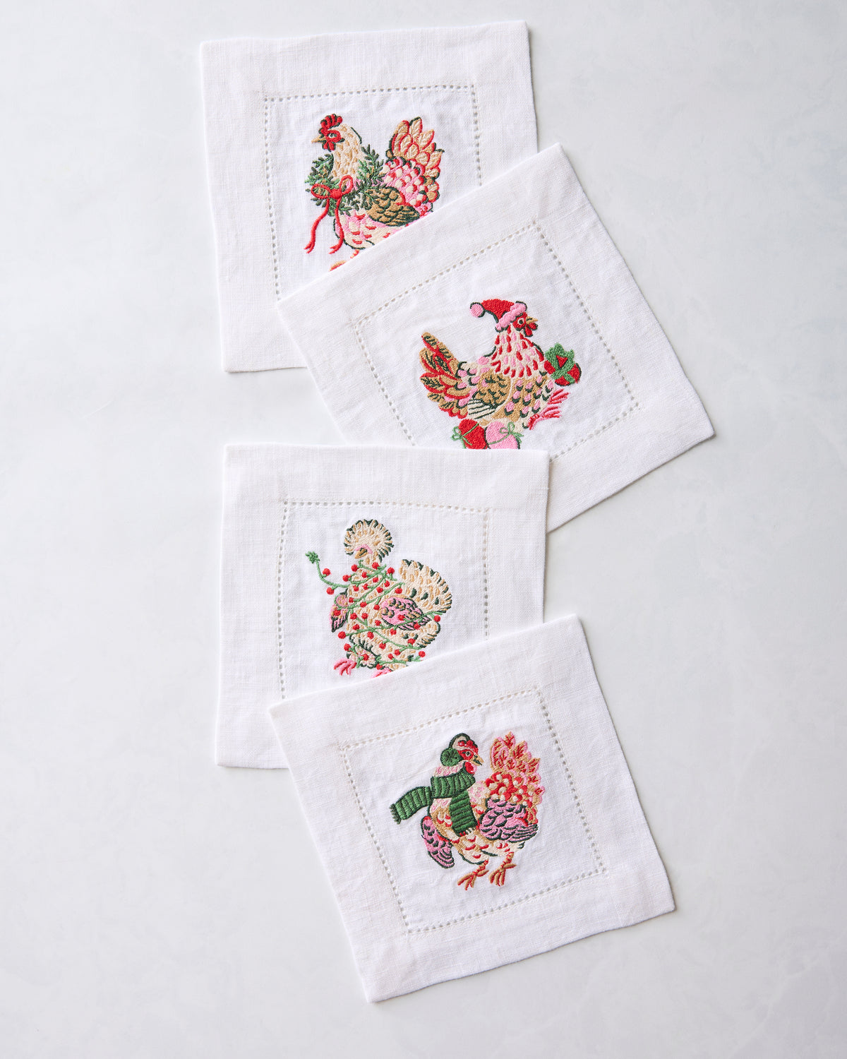 Four embroidered chicken cocktail napkins overlapping in a diagonal arrangement
