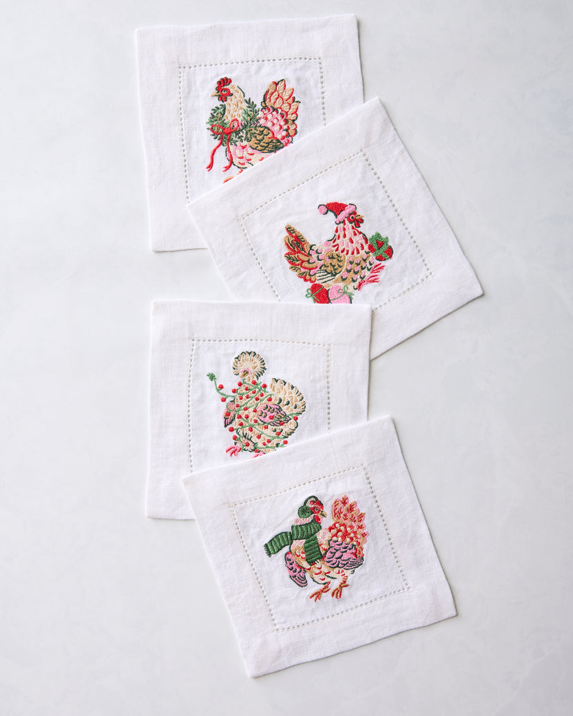 Four embroidered chicken cocktail napkins overlapping in a diagonal arrangement