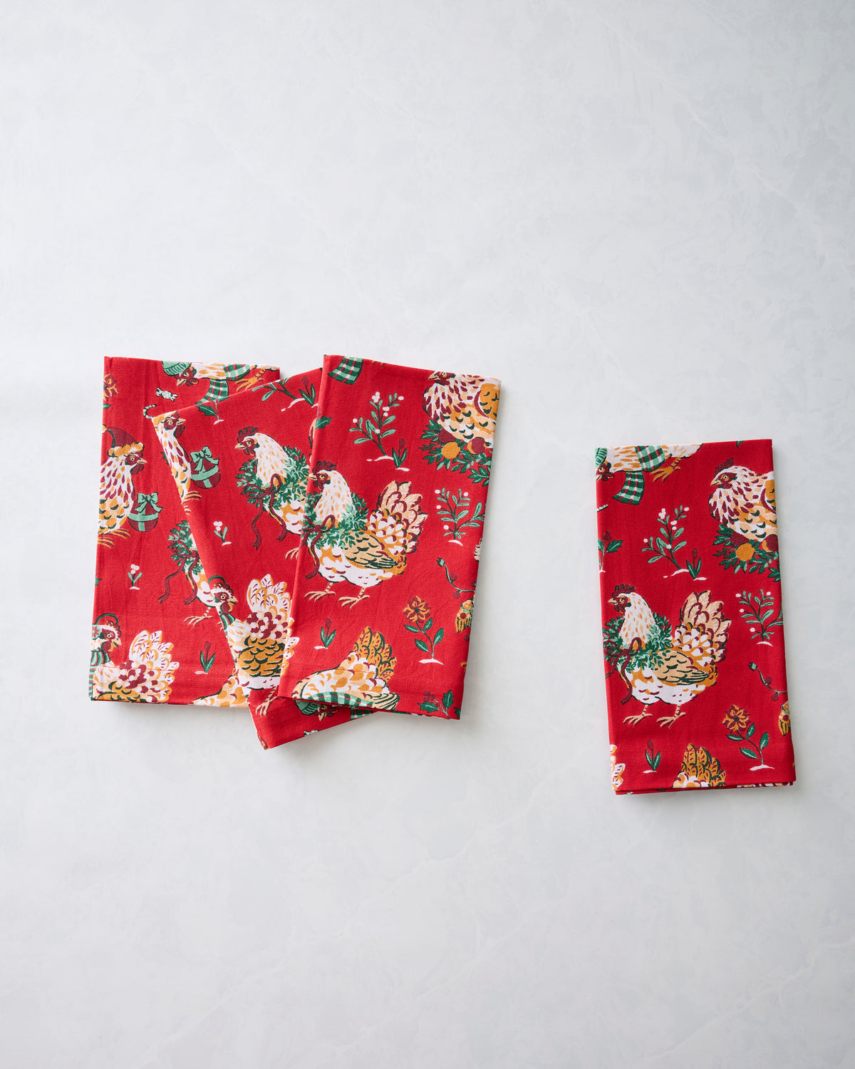 Two red dinner napkins with a holiday hen and floral print, including a separate folded napkin at right.