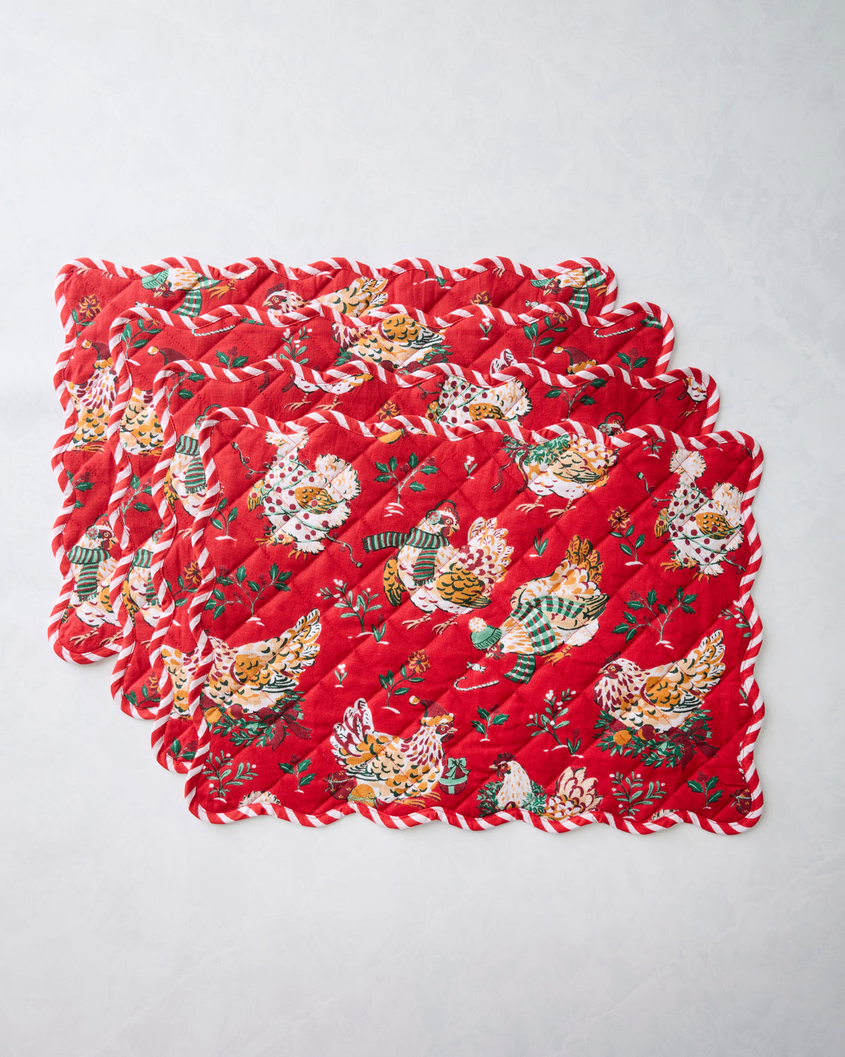Four overlapping red scalloped placemats with a quilted pattern and illustrated hens wearing patterned clothing.