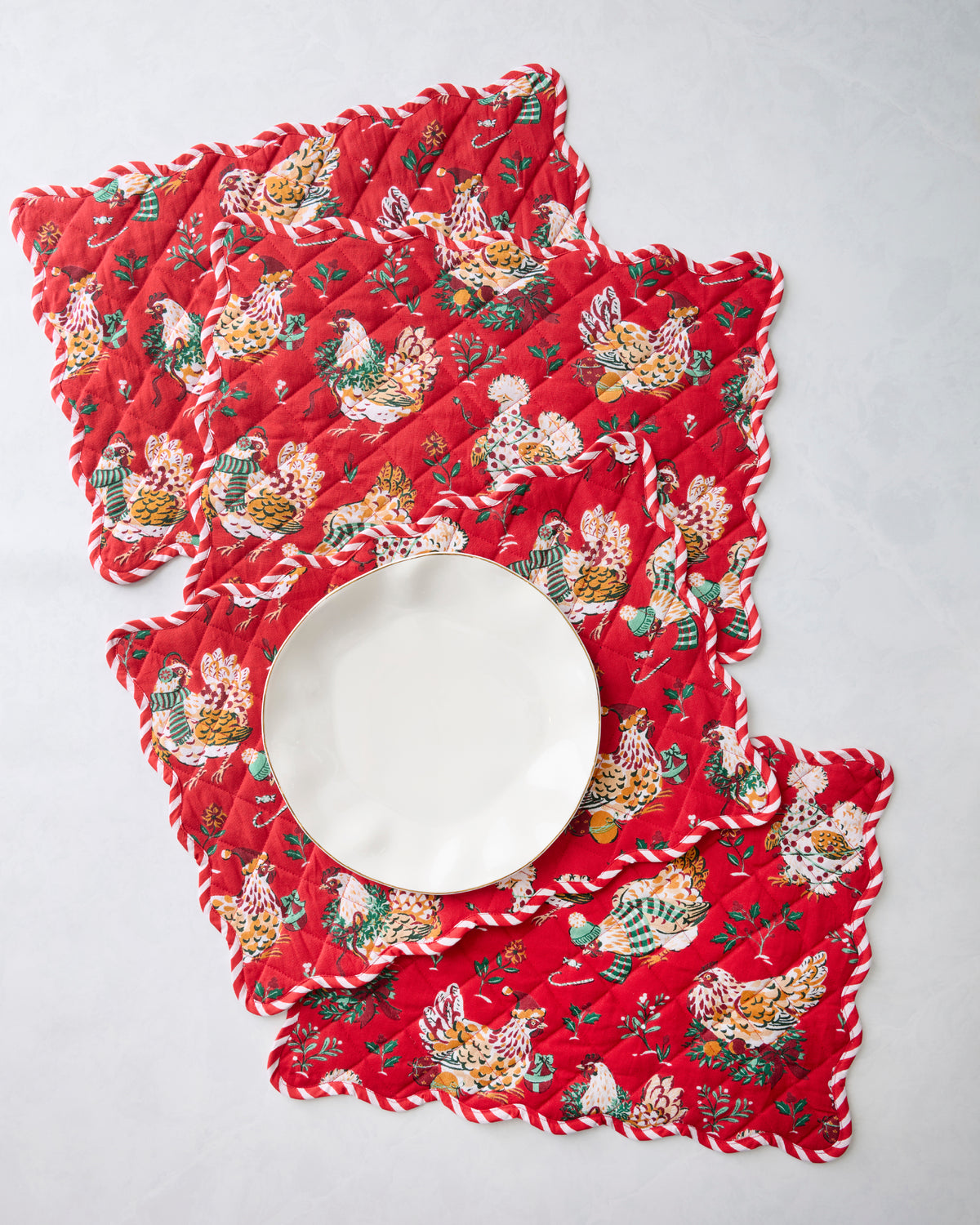 Four red scalloped placemats with an illustrated hen print, arranged with a white plate on top.