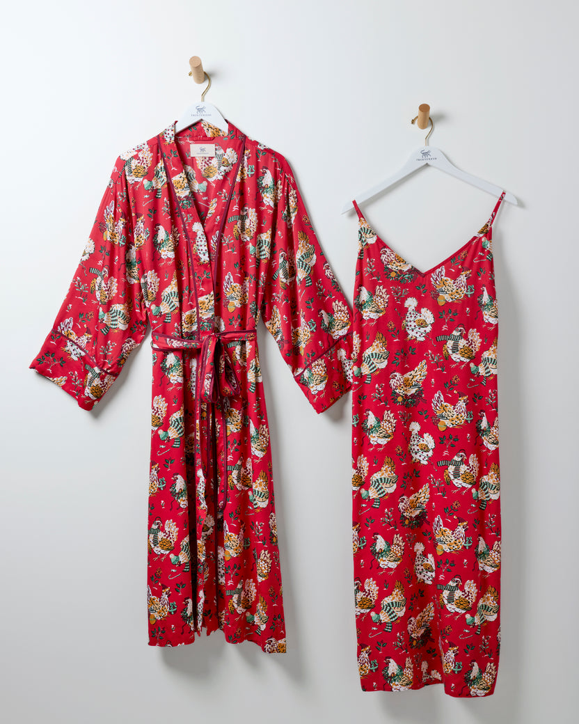 Red holiday hen-print robe with belt beside a matching sleeveless nightie, both hanging on hooks.