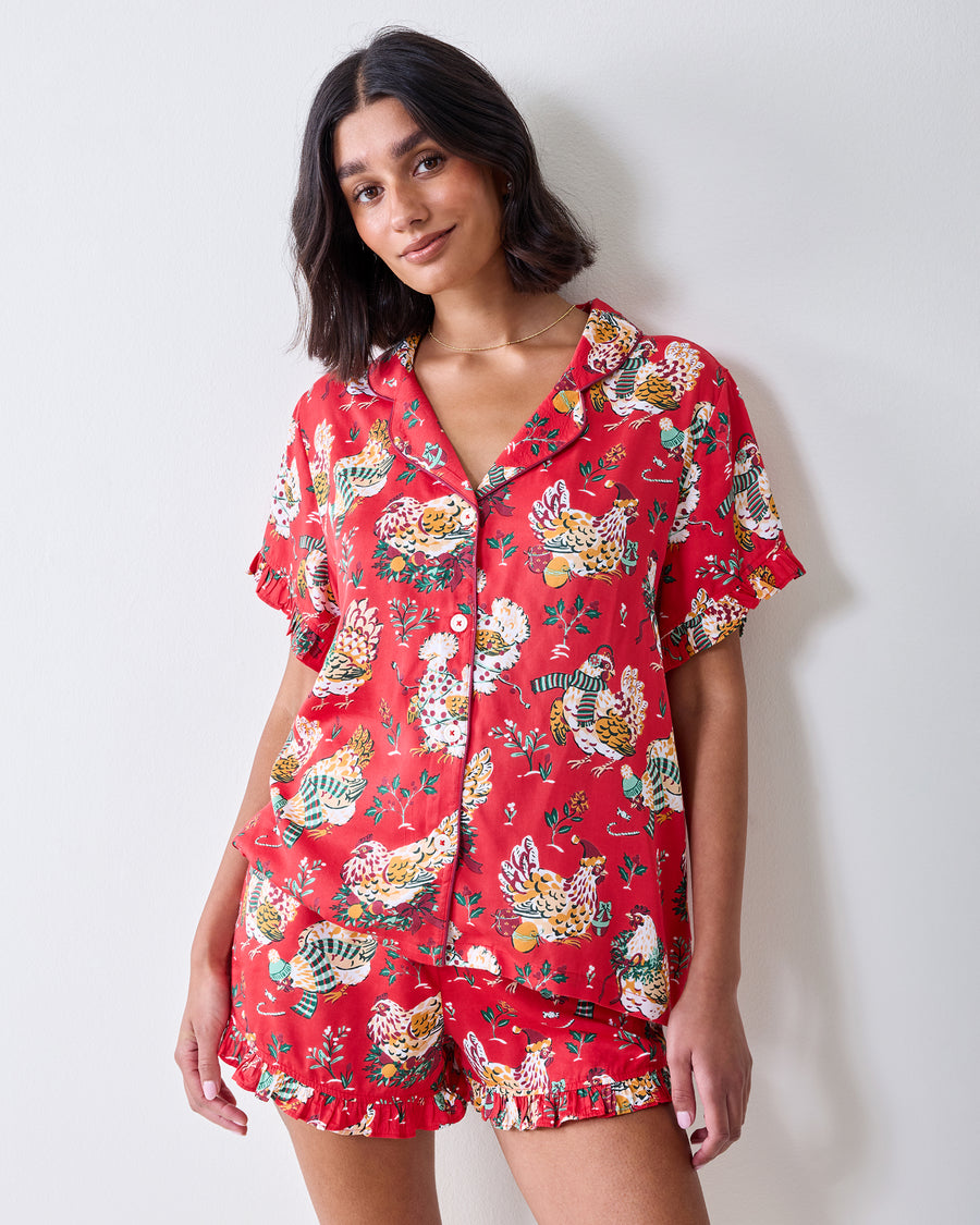 Front view of a model wearing the red Holiday Hens short pajama set with ruffled sleeves, button-front top, and chicken print.