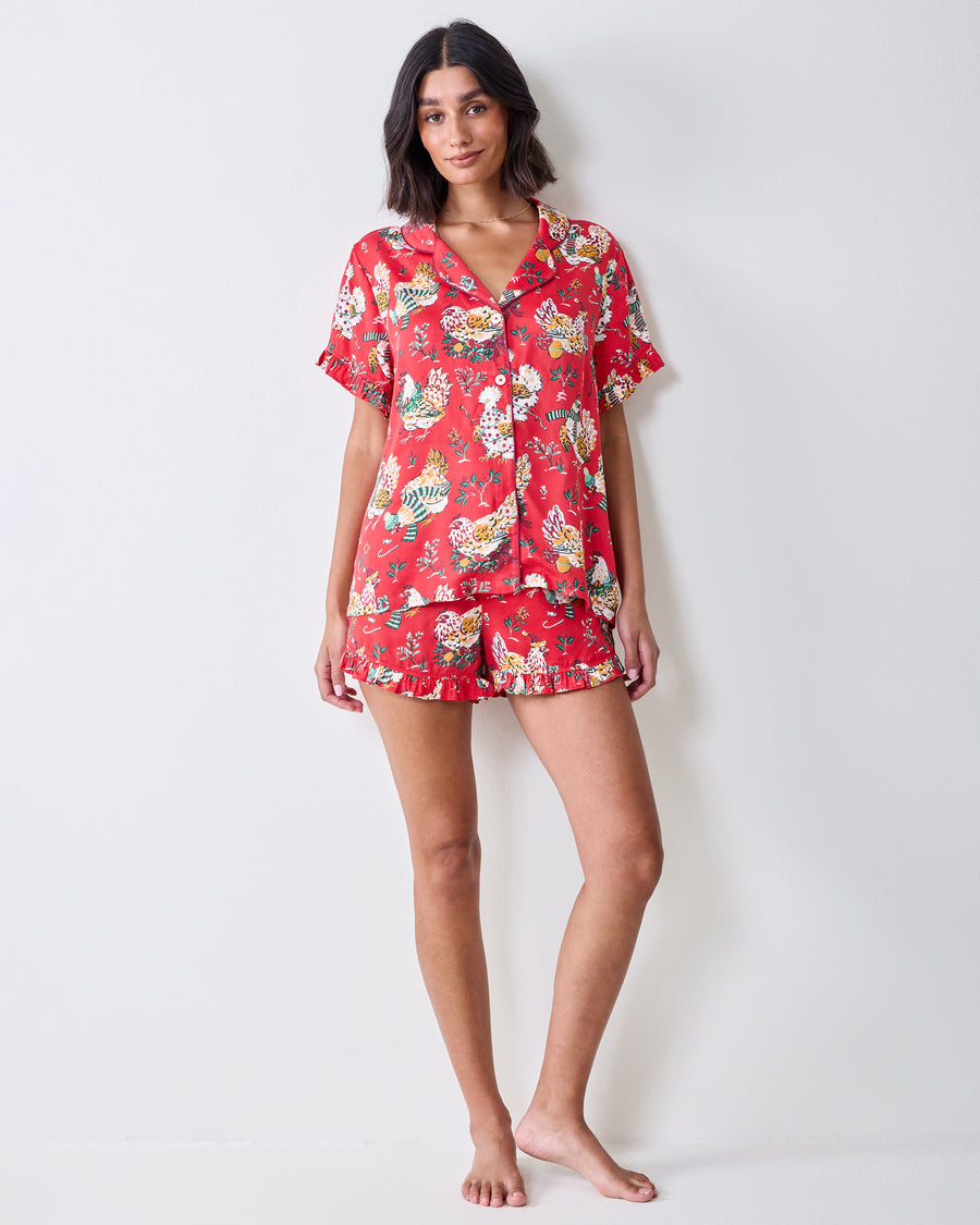 Full-length front view of a model wearing the red Holiday Hens short pajama set with ruffled trim and chicken print.