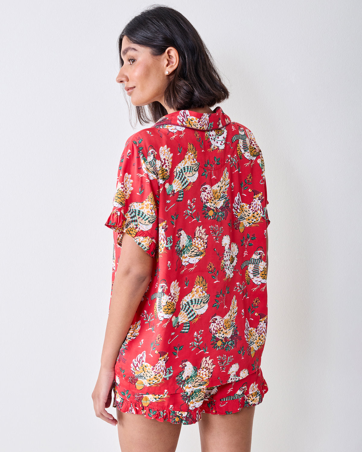 Back view of a model wearing the red Holiday Hens short pajama set with ruffled trim and chicken print.