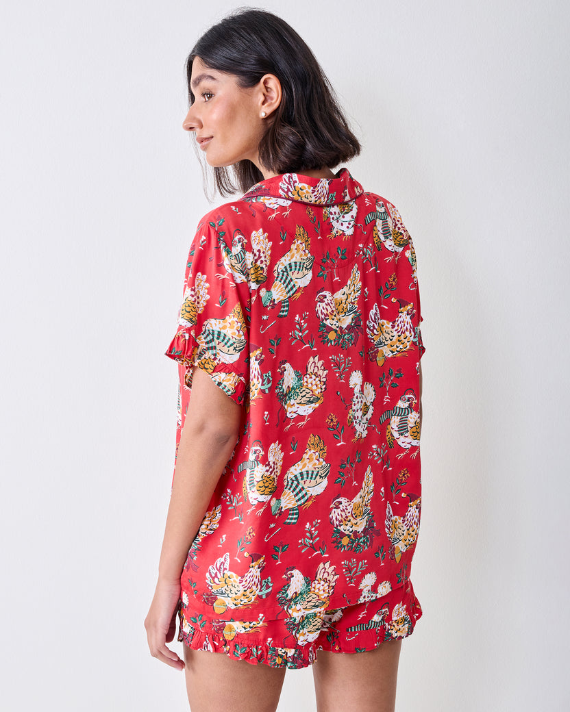 Back view of a model wearing the red Holiday Hens short pajama set with ruffled trim and chicken print.