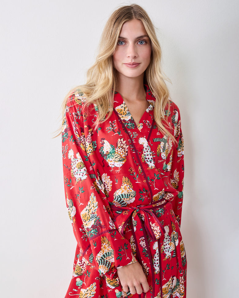 Person standing and wearing a red holiday hen-print robe with long sleeves and a waist tie.