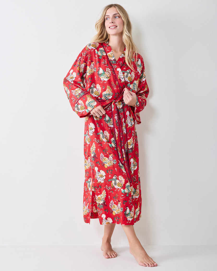 Person standing in a red holiday hen-print robe with a shawl collar, long sleeves, waist tie, and below-knee length.