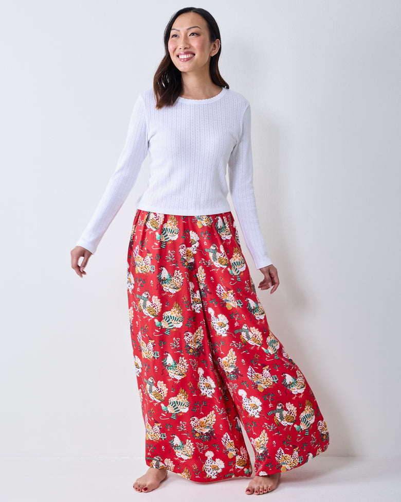 Front three-quarter view of a model wearing red Holiday Hens wide-leg pants with an all-over chicken and floral print.