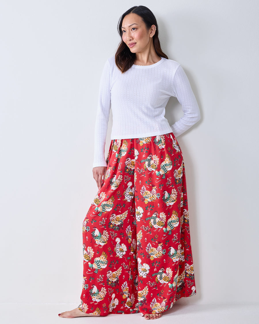 Full-length front view of a model wearing red Holiday Hens wide-leg pants with an all-over chicken and floral print.