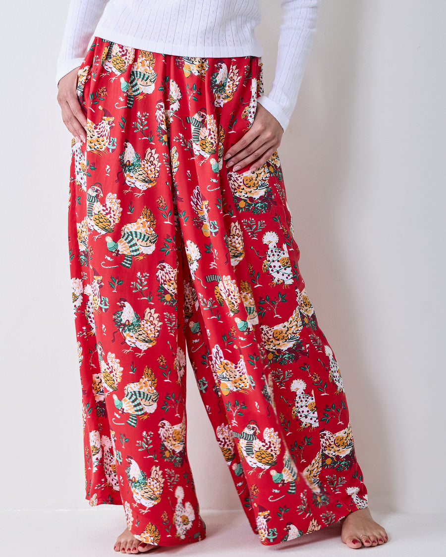 Close-up of red Holiday Hens wide-leg pants with an all-over chicken and floral print, worn with a white top.