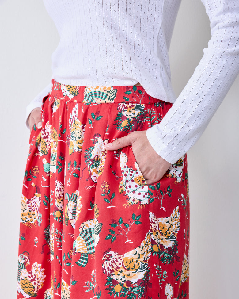 Close-up front view of red Holiday Hens pants with a colorful hen print and a hand in the side pocket.