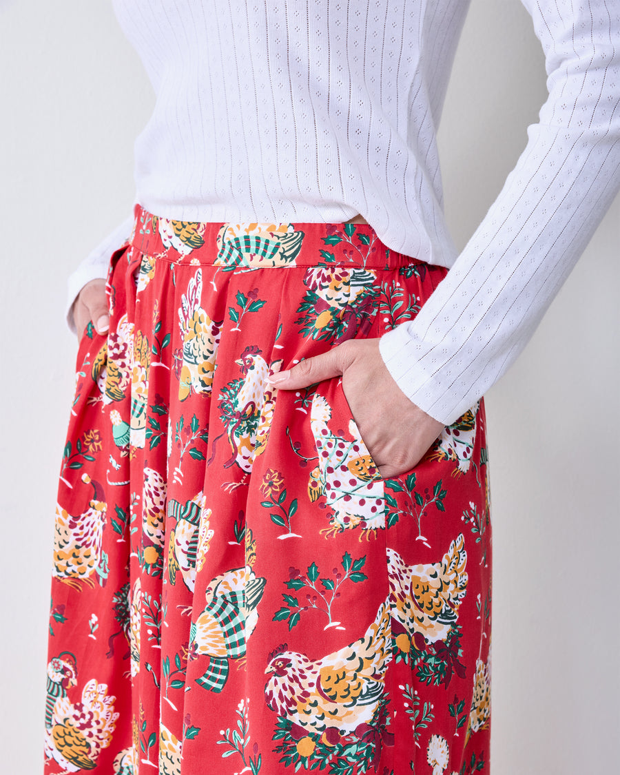 Close-up front view of red Holiday Hens pants with a colorful hen print and a hand in the side pocket.