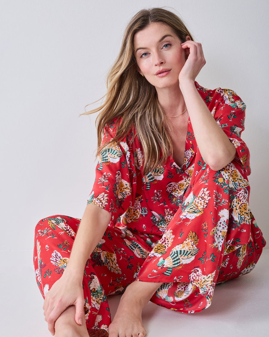 Person seated wearing the red Holiday Hens pajama set with a printed top and pants.
