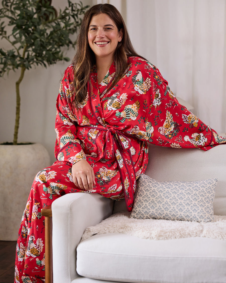 Person seated on a sofa wearing a red holiday hen-print robe with a waist tie and long sleeves.