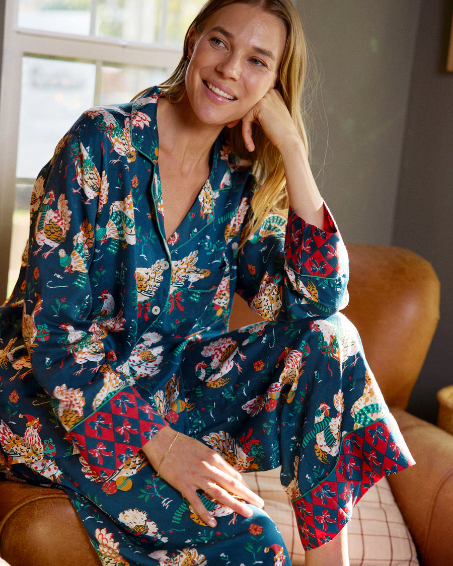 Model seated in a navy pajama set with a festive hen print and contrasting red patterned cuffs.