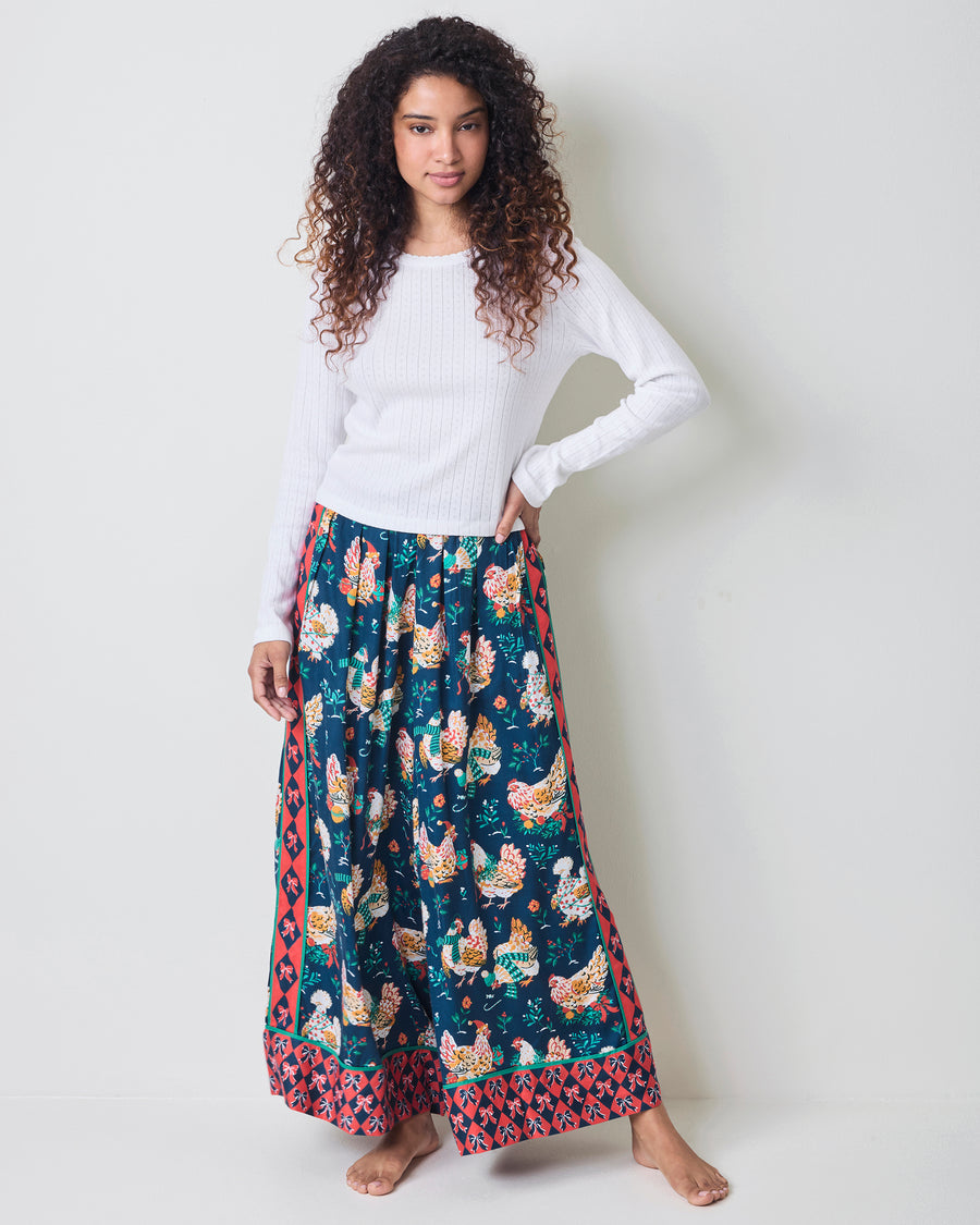 Person wearing the full-length Holiday Hens satin pants with a dark blue chicken print and red patterned border.