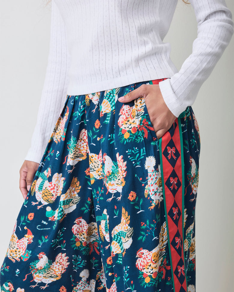 Close view of the Holiday Hens satin pants showing the gathered waistband, side pocket, chicken print, and red patterned stripe.