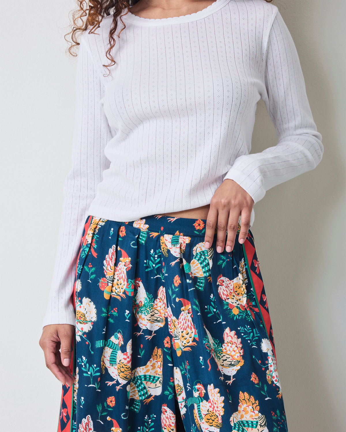 Close view of the Holiday Hens satin pants showing the elastic waistband, dark blue chicken print, and red patterned side stripe.