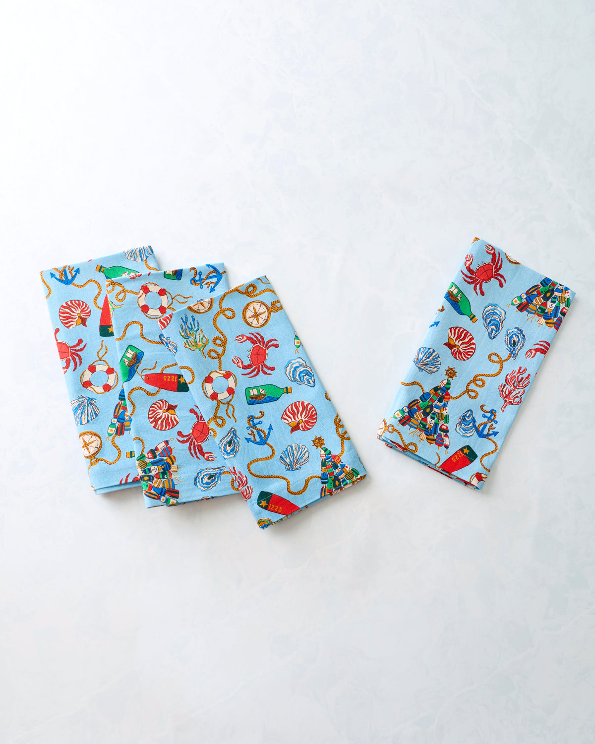 Four folded dinner napkins arranged separately, showing the blue nautical Christmas print.