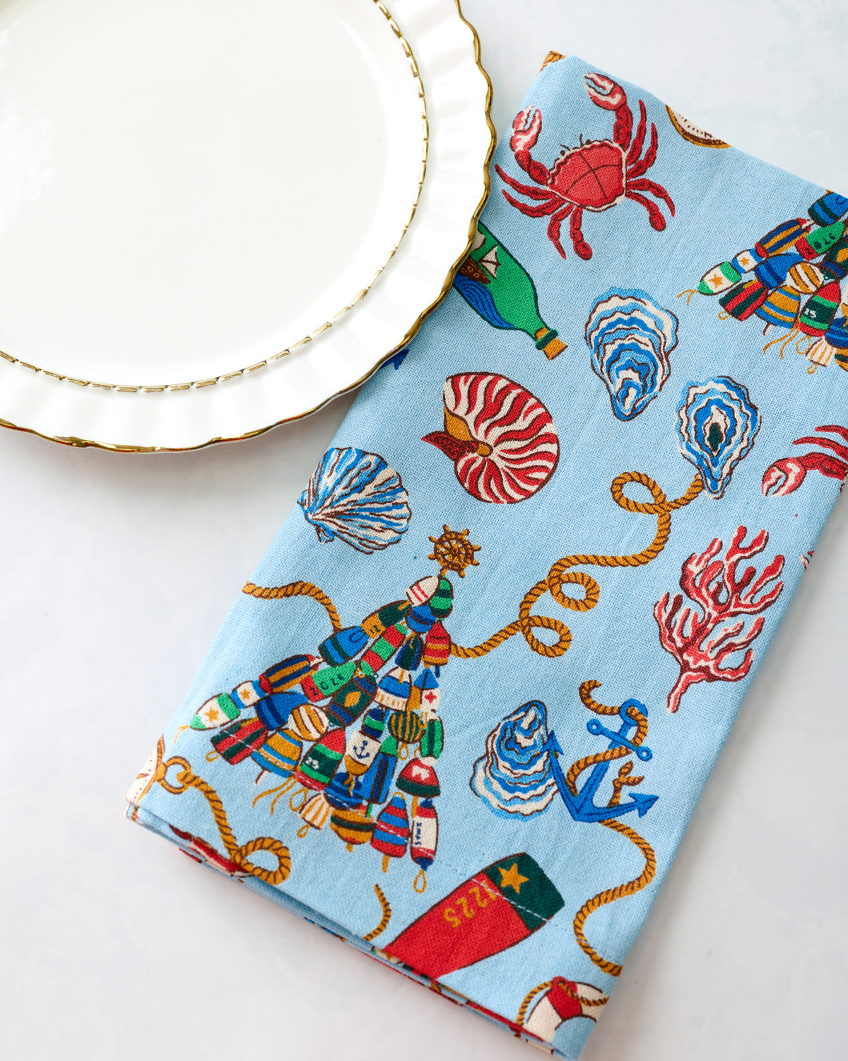 Close-up of a blue printed dinner napkin beside a white plate with a gold rim.