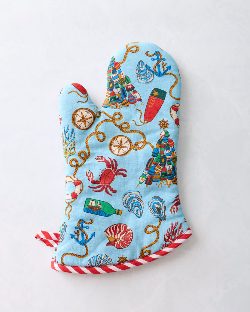 Opposite side of a blue printed oven mitt with nautical Christmas motifs and red-and-white striped trim.