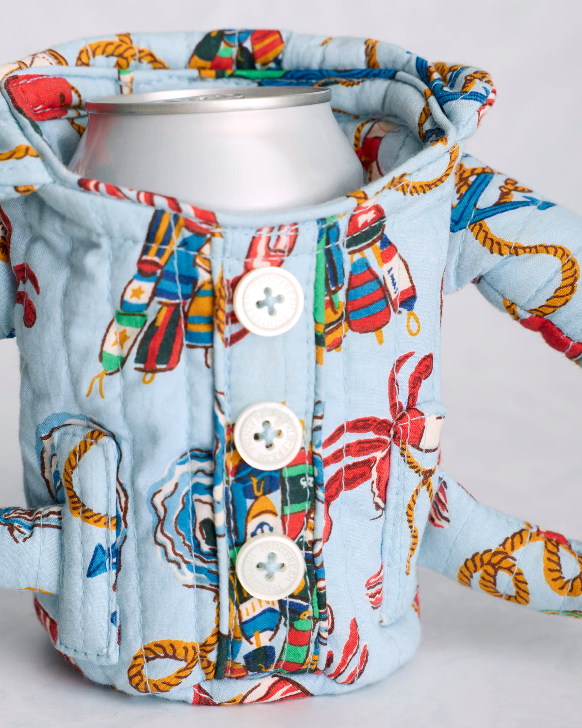 Close-up of the blue patterned pajama cozie holding a beverage can, showing its buttons, handles, and quilted construction
