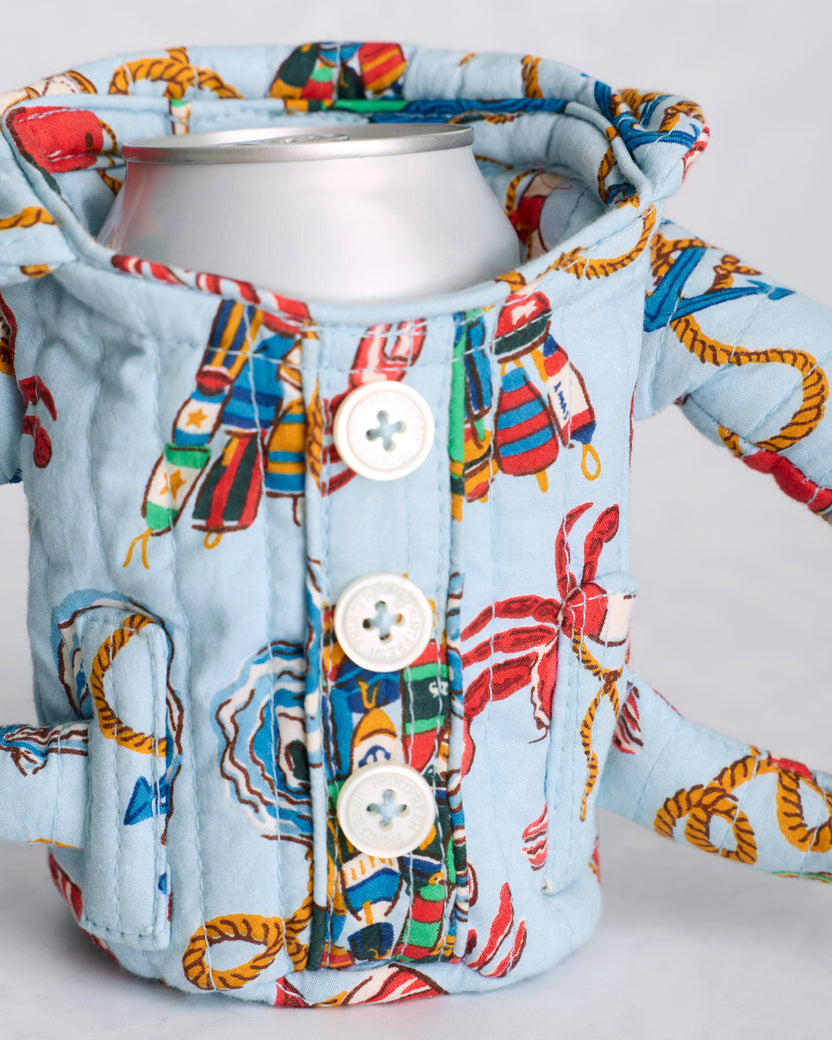 Close-up of the blue patterned pajama cozie holding a beverage can, showing its buttons, handles, and quilted construction