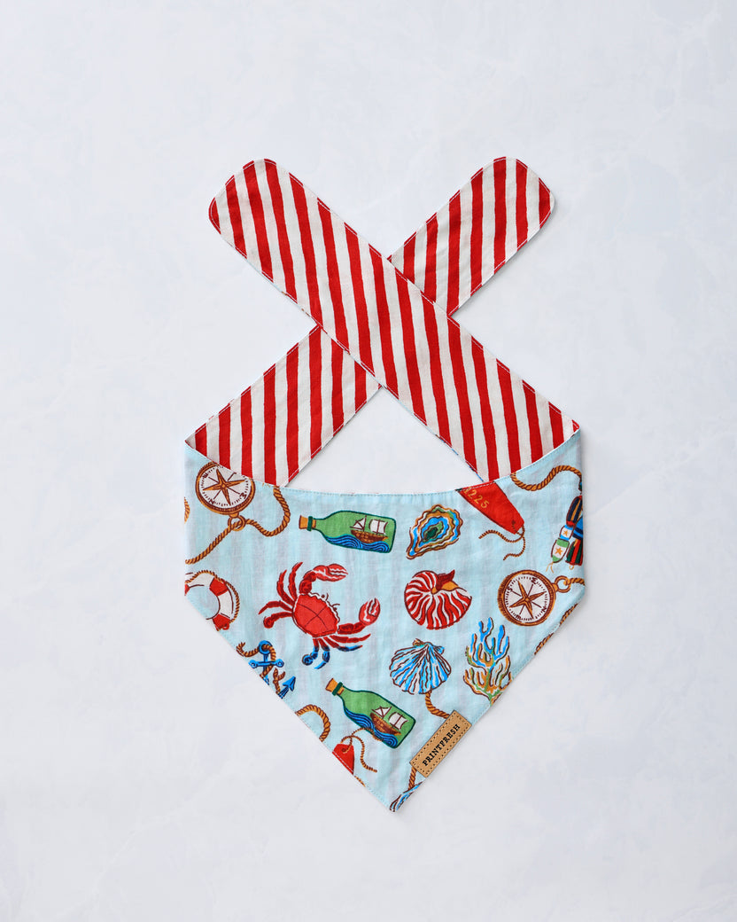 Pet bandana laid flat with a pale blue nautical print and red-and-white striped ties.