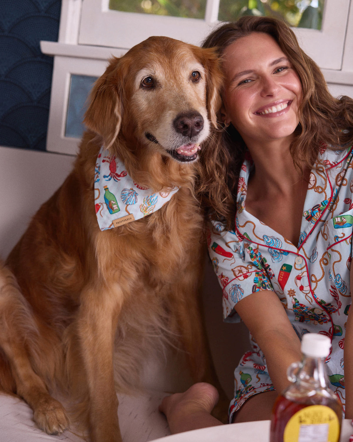 Dog wearing a pale blue nautical-print bandana beside a person wearing matching patterned pajamas.