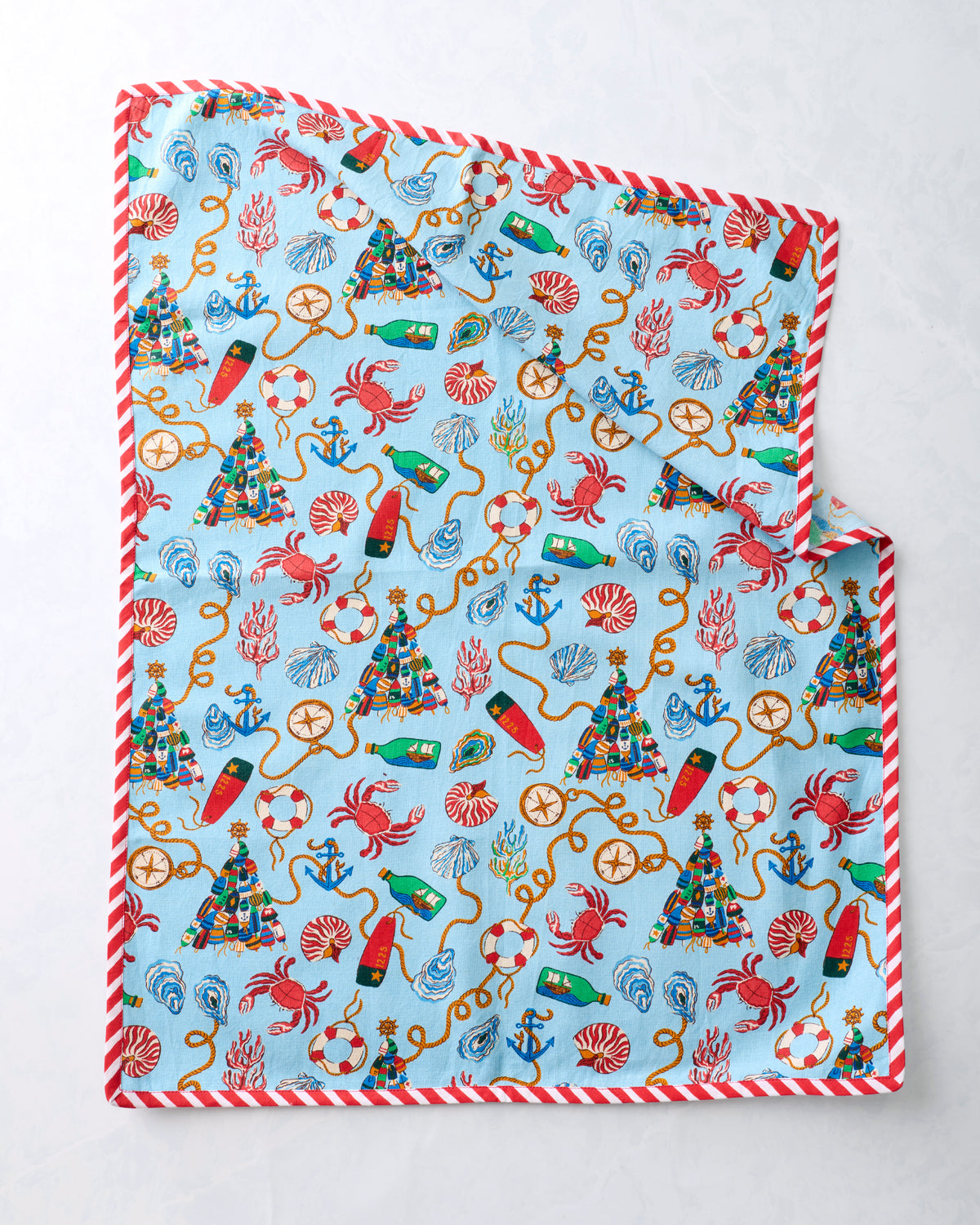 Tea towel spread flat to display the repeating blue nautical Christmas print and red-and-white striped trim.