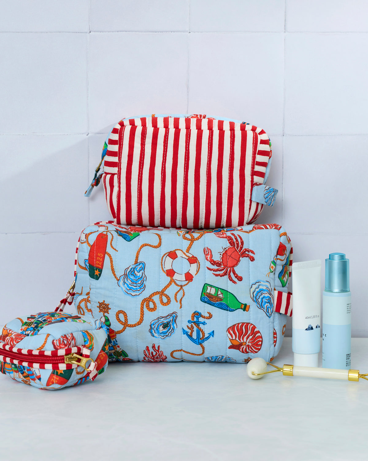 Three patterned pouches displayed with toiletries; the set includes pale blue nautical-print pouches and a red-and-white striped pouch.